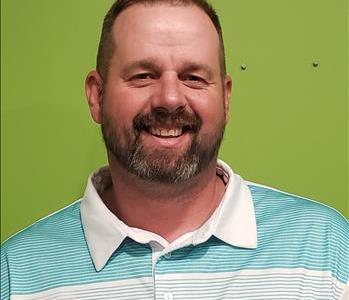 SERVPRO employee on a green background wearing a white and blue shirt