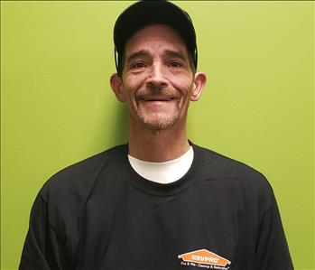 Male SERVPRO employee in uniform standing against a green background