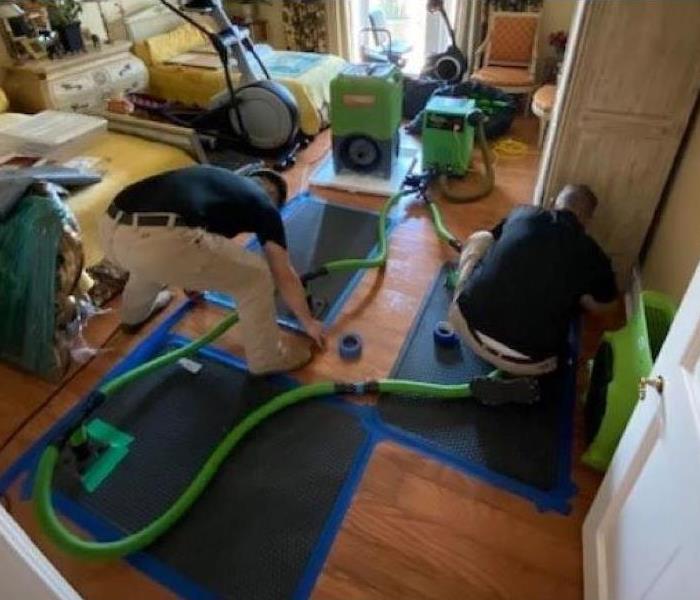 Men setting up drying mats on wood flooring in a water damaged home in Callaway near me