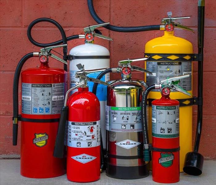 A variety of fire extinguishers in front of a red wall